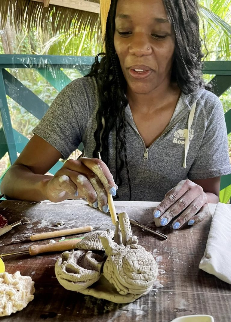 A woman shaping a clay model of coral at a wooden table.