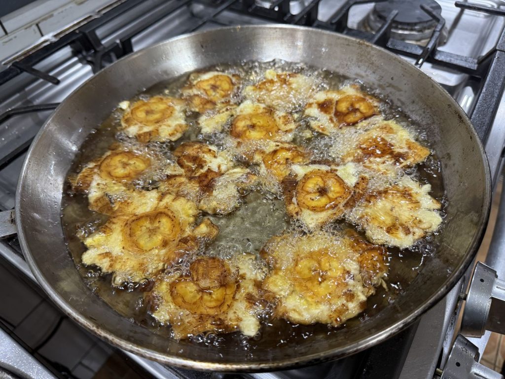 Slices of plantain frying in a wide pan on the stove