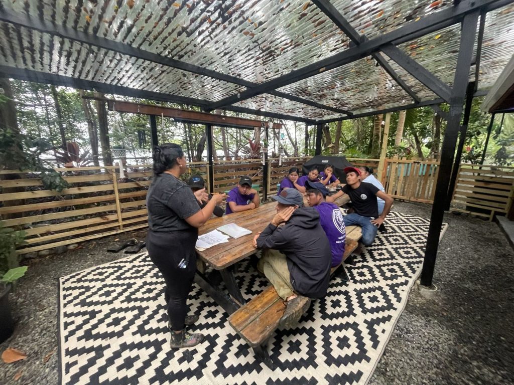 Members of the team seated around a long table under a shaded shelter in the garden