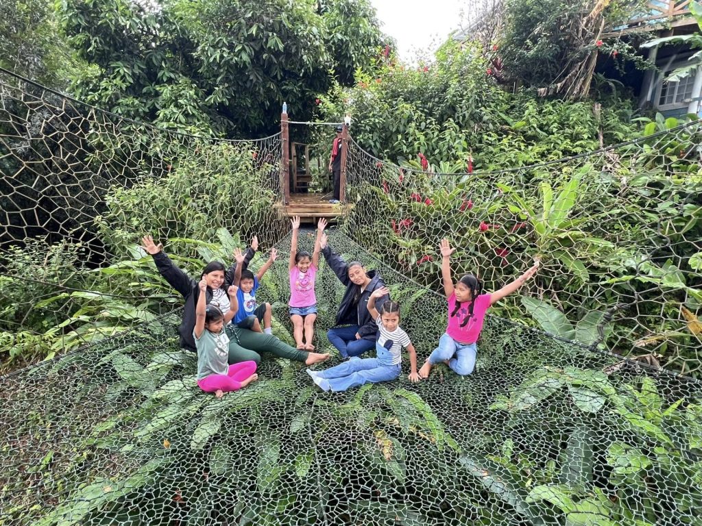 Children and adults with their arms raised, sitting on the tree net in the forest canopy.